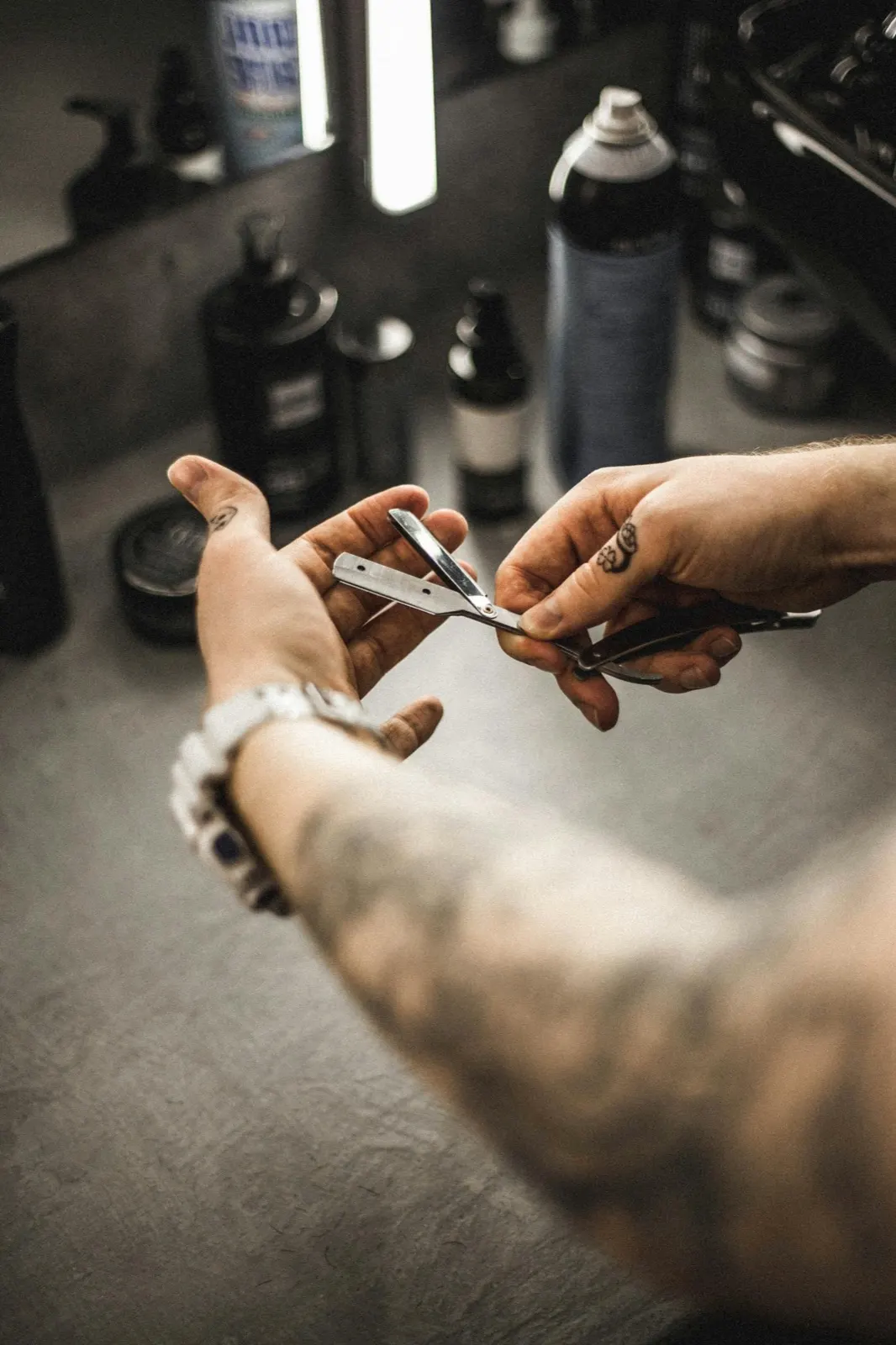 Tattooed barber's hand with a straight razor